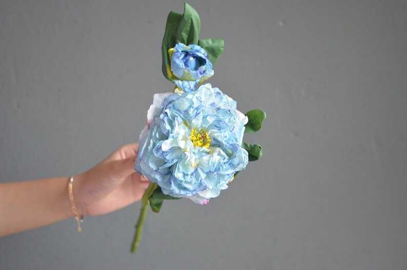 May include: A single stem artificial flower with a large blue and white flower and a smaller blue flower bud. The flower has a yellow center.
