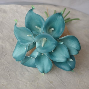 Op de afbeelding: Een boeket van teal kunstmatige calla lelies. De bloemen zijn in een cluster gerangschikt en hebben een gladde, glanzende afwerking.