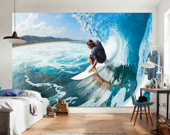 Puede incluir: Un surfista monta una ola grande, el agua es de un azul y verde vibrantes. El surfista lleva una camisa azul oscuro y está en el aire sobre una tabla de surf blanca.