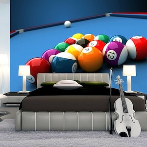 May include: A bedroom with a blue pool table mural on the wall. The mural features a group of billiard balls in various colors, including red, yellow, green, blue, and black. The balls are arranged in a triangle formation, with the white cue ball at the top. A bed with a black headboard and a brown comforter is in front of the mural. A violin is leaning against the bed, and a lamp is on a side table next to the bed.