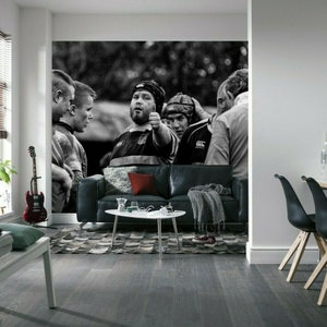 Può includere: Foto in bianco e nero di un gruppo di giocatori di rugby in un gruppo. I giocatori indossano maglie e caschi. La foto è stampata su un murale.