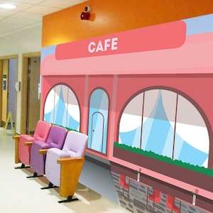 以下が含まれることがあります： 病院の壁に「CAFE」と書かれたピンクと白の漫画のカフェの壁画。壁画の前に紫とピンクの椅子が3つある。