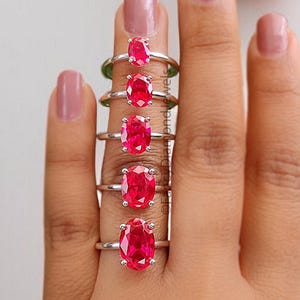 Könnte beinhalten: Ein Satz von sieben ovalen Rubinringen in verschiedenen Größen, auf einer Hand präsentiert.