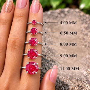 May include: Five silver rings featuring round, vibrant red stones in prong settings. The rings are displayed in ascending order of size, labeled with measurements of 4.00 MM, 6.50 MM, 8.00 MM, 9.00 MM, and 11.00 MM to indicate the stone diameter.