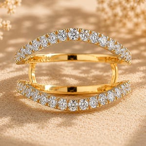 May include: A gold ring featuring a double-band design with an open gap between the two curved sections. Both bands are adorned with a continuous row of small, round, clear, faceted stones set along the outer edges of the gold metal frame.