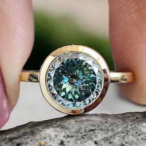 May include: A gold ring with a large, round, bezel-set blue-green gemstone. The ring has a simple band and a wide, polished bezel.