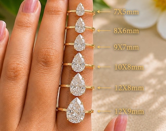 May include: A collection of six gold rings featuring pear-cut clear stones in varying sizes. The rings are labeled with dimensions: 7x5mm, 8x6mm, 9x7mm, 10x8mm, 12x8mm, and 12x9mm. Each ring has a thin gold band and a single faceted pear-shaped stone.
