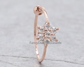 Può includere: Un anello per il naso in oro rosa con una montatura a forma di fiore di piccoli diamanti trasparenti. L'anello è aperto e ha una piccola sfera all'estremità.