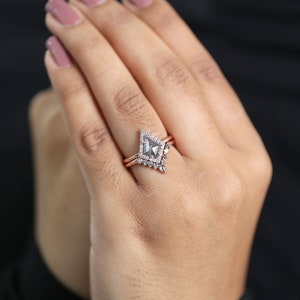 May include: A rose gold engagement ring set with a gray kite-shaped center stone and a diamond halo. The set includes a matching band with small diamonds. The ring is shown on a hand with pink nail polish.