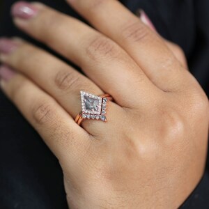 May include: A rose gold engagement ring set featuring a kite-shaped gray diamond center stone, surrounded by a halo of smaller diamonds. The set includes a matching band with delicate diamond accents. The ring is displayed on a hand.