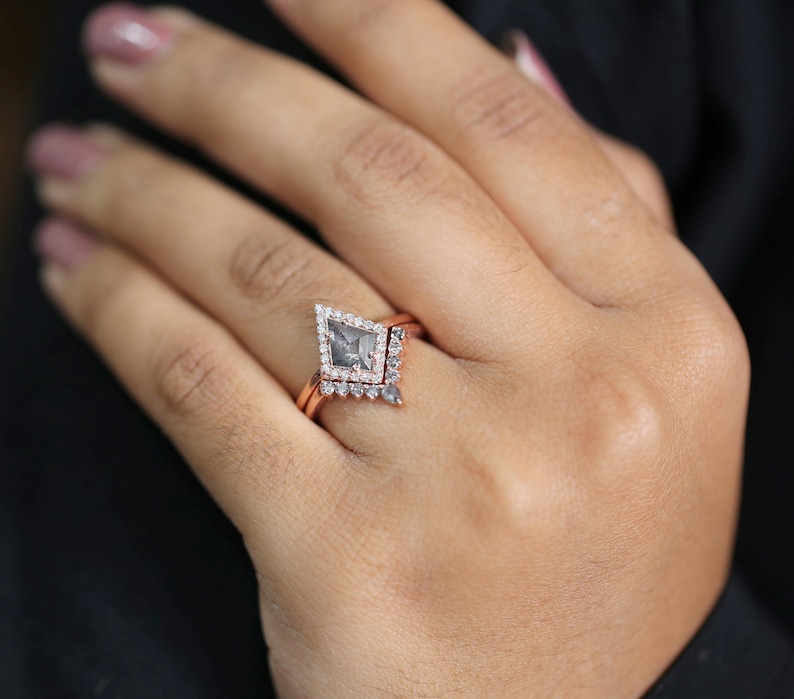 May include: A rose gold engagement ring set featuring a kite-shaped gray diamond center stone, surrounded by a halo of smaller diamonds. The set includes a matching band with delicate diamond accents. The ring is displayed on a hand.