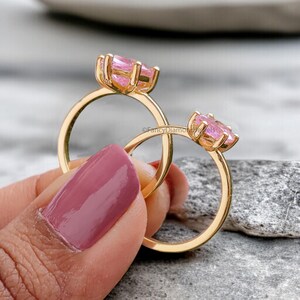 Puede incluir: Dos anillos de oro con engastes de piedras preciosas rosas. Los anillos est&aacute;n apilados uno encima del otro y est&aacute;n siendo sostenidos por una mano.