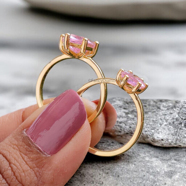 Puede incluir: Dos anillos de oro con engastes de piedras preciosas rosas. Los anillos est&aacute;n apilados uno encima del otro y est&aacute;n siendo sostenidos por una mano.