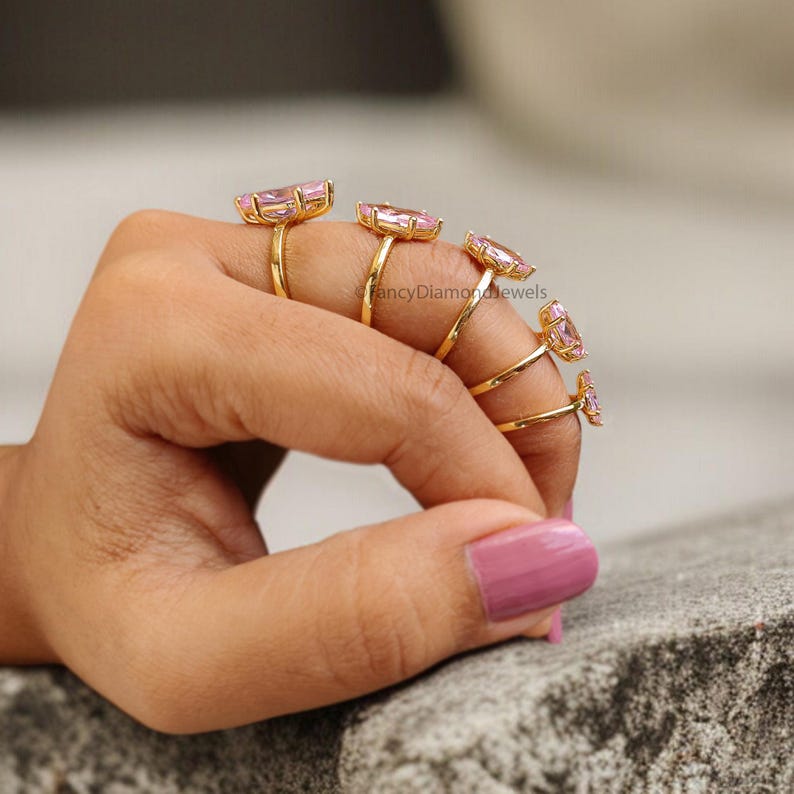 Puede incluir: Cinco anillos de oro con piedras preciosas rosas. Los anillos est&aacute;n apilados en un dedo, con el anillo m&aacute;s grande en la parte inferior y el anillo m&aacute;s peque&ntilde;o en la parte superior.