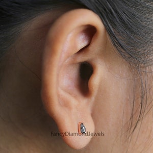 Puede incluir: Primer plano de una oreja con un peque&ntilde;o pendiente de diamante negro. El pendiente est&aacute; engastado en un engaste de oro rosa. El texto "FancyDiamondJewels" es visible debajo del pendiente.