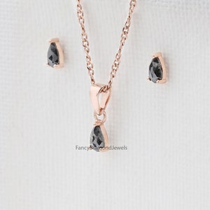 Puede incluir: Un collar con colgante de diamante negro en forma de pera y pendientes a juego en oro rosa. El collar presenta una cadena delicada y un dise&ntilde;o de colgante simple. Los pendientes son de estilo de bot&oacute;n con un peque&ntilde;o diamante en forma de pera.