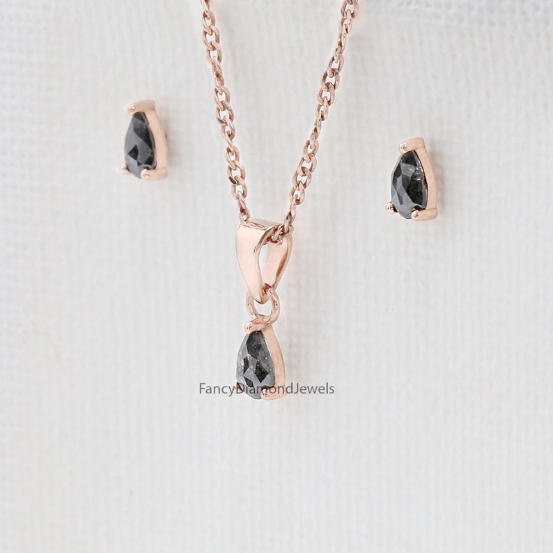 Puede incluir: Un collar con colgante de diamante negro en forma de pera y pendientes a juego en oro rosa. El collar presenta una cadena delicada y un dise&ntilde;o de colgante simple. Los pendientes son de estilo de bot&oacute;n con un peque&ntilde;o diamante en forma de pera.