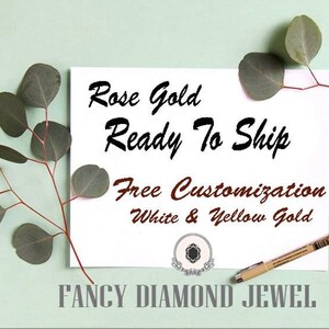 Puede incluir: Una tarjeta blanca con el texto "Rose Gold Ready To Ship Free Customization White & Yellow Gold" y el logotipo "FANCY DIAMOND JEWEL". La tarjeta est&aacute; sobre un fondo verde claro con hojas de eucalipto.