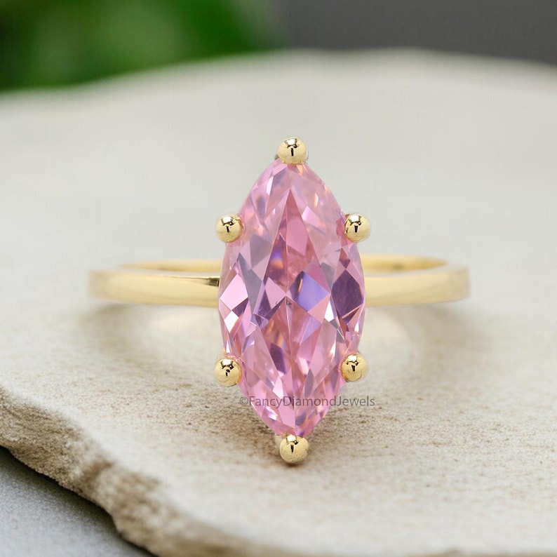 Puede incluir: Un anillo de oro con una piedra preciosa rosa en forma de marquesa. El anillo est&aacute; engastado con peque&ntilde;os detalles dorados alrededor de la piedra preciosa.