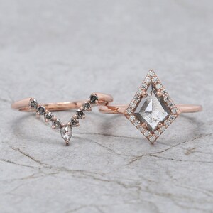 May include: Two rose gold rings. One ring features a kite-shaped, gray-toned center stone surrounded by small white diamonds. The second ring has a curved design with a series of small, gray stones.