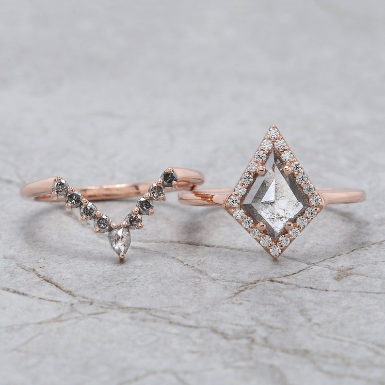May include: Two rose gold rings. One ring features a kite-shaped, gray-toned center stone surrounded by small white diamonds. The second ring has a curved design with a series of small, gray stones.