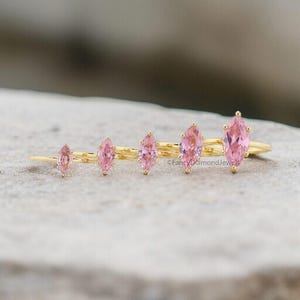 Puede incluir: Cinco anillos de oro con piedras preciosas de forma marquesa rosa. Los anillos est&aacute;n dispuestos en orden de tama&ntilde;o, con el anillo m&aacute;s grande a la izquierda y el m&aacute;s peque&ntilde;o a la derecha.