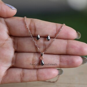 Puede incluir: Un collar con colgante de diamante negro y pendientes a juego en oro rosa. El colgante tiene forma de pera y los pendientes son peque&ntilde;os y redondos. El collar es delicado y tiene una cadena sencilla.