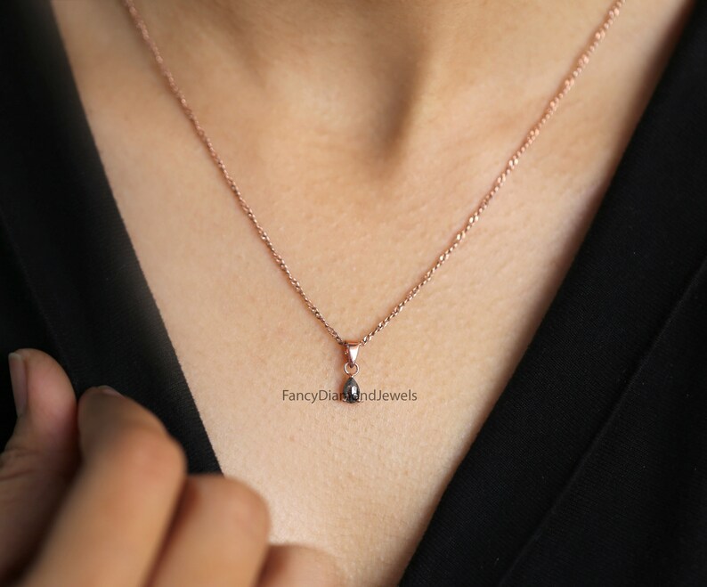 Puede incluir: Un delicado collar de cadena de oro rosa con un peque&ntilde;o colgante de l&aacute;grima negra. El colgante est&aacute; engastado con un solo diamante negro. "FancyDiamondsAndJewels" est&aacute; impreso debajo del colgante.