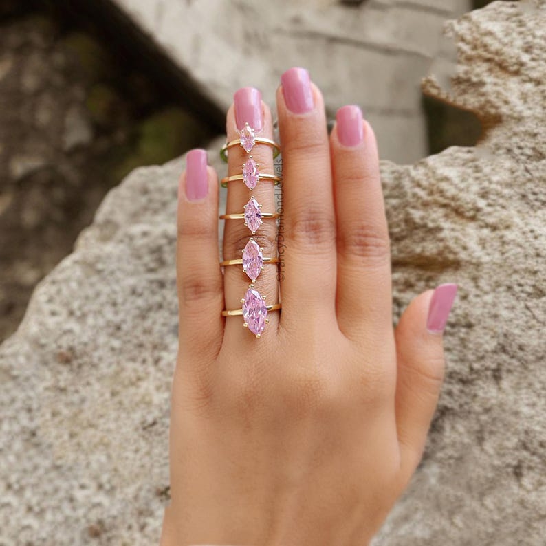 Puede incluir: Un conjunto de cinco anillos de oro con piedras preciosas de color rosa en forma de marquesa. Los anillos est&aacute;n ordenados por tama&ntilde;o, con el anillo m&aacute;s grande a la izquierda y el m&aacute;s peque&ntilde;o a la derecha.