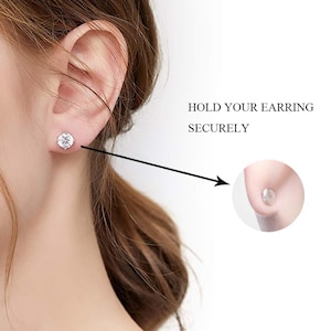 May include: An ear with a clear, round earring is shown. The text reads "HOLD YOUR EARRING SECURELY". A magnified view shows a clear earring back. The earring is a stud with a clear, round stone.