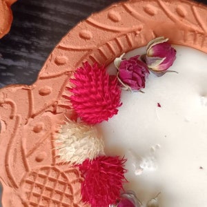 May include: A terracotta candle holder with a white candle and dried flowers. The holder has a decorative design and is shaped like a heart.