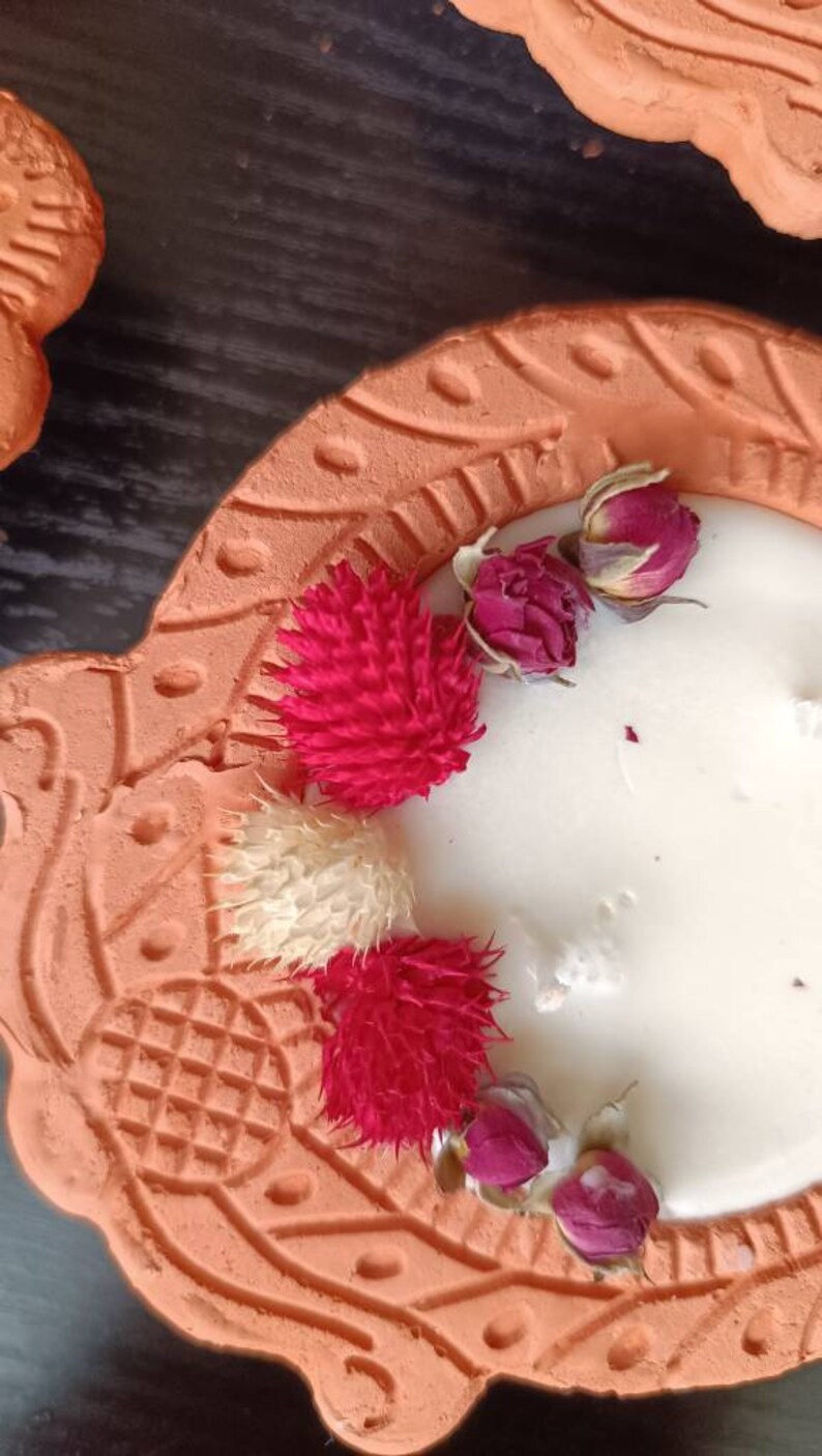 May include: A terracotta candle holder with a white candle and dried flowers. The holder has a decorative design and is shaped like a heart.