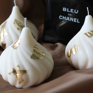 May include: Three white candles with gold leaf accents. The candles are shaped like a teardrop and have a swirl design.