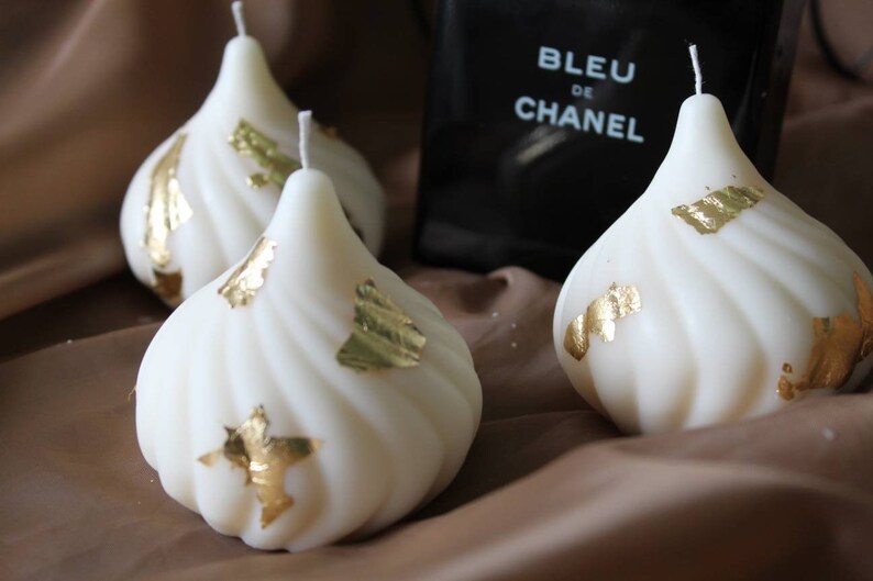 May include: Three white candles with gold leaf accents. The candles are shaped like a teardrop and have a swirl design.