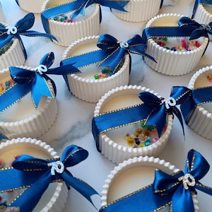 May include: White, round, fluted containers filled with a clear gel and colorful confetti. Each container is adorned with a navy blue ribbon tied into a bow, with a silver "70" charm. The containers are arranged on a white surface.