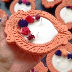 May include: A set of terracotta candle holders with white candles and dried flowers. The holders are decorated with intricate designs and have a rustic look.