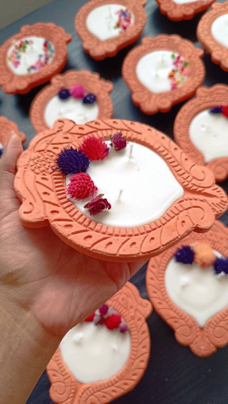 May include: A set of terracotta candle holders with white candles and dried flowers. The holders are decorated with intricate designs and have a rustic look.