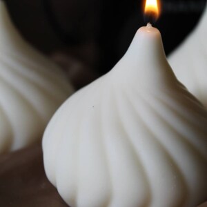 May include: A white, swirl-shaped candle with a single flame burning at the top. The candle is sitting on a brown surface.