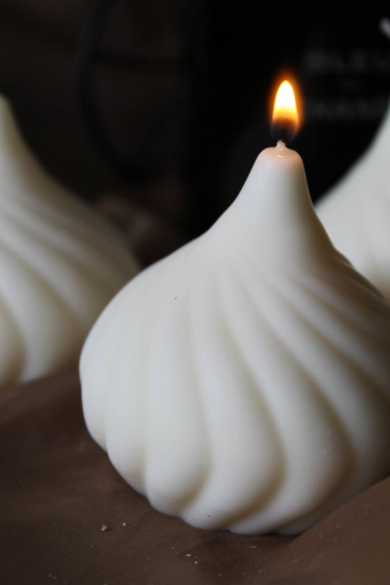 May include: A white, swirl-shaped candle with a single flame burning at the top. The candle is sitting on a brown surface.