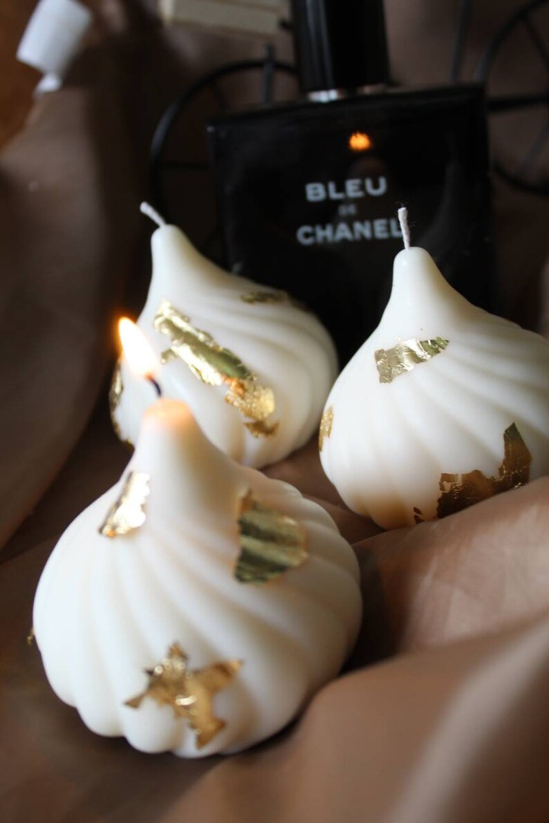 May include: Three white swirl candles with gold leaf accents. The candles are shaped like a pear or teardrop.
