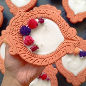May include: A collection of terracotta candle holders with white candles and dried flower accents. The holders are decorated with intricate designs and have a rustic, earthy aesthetic.