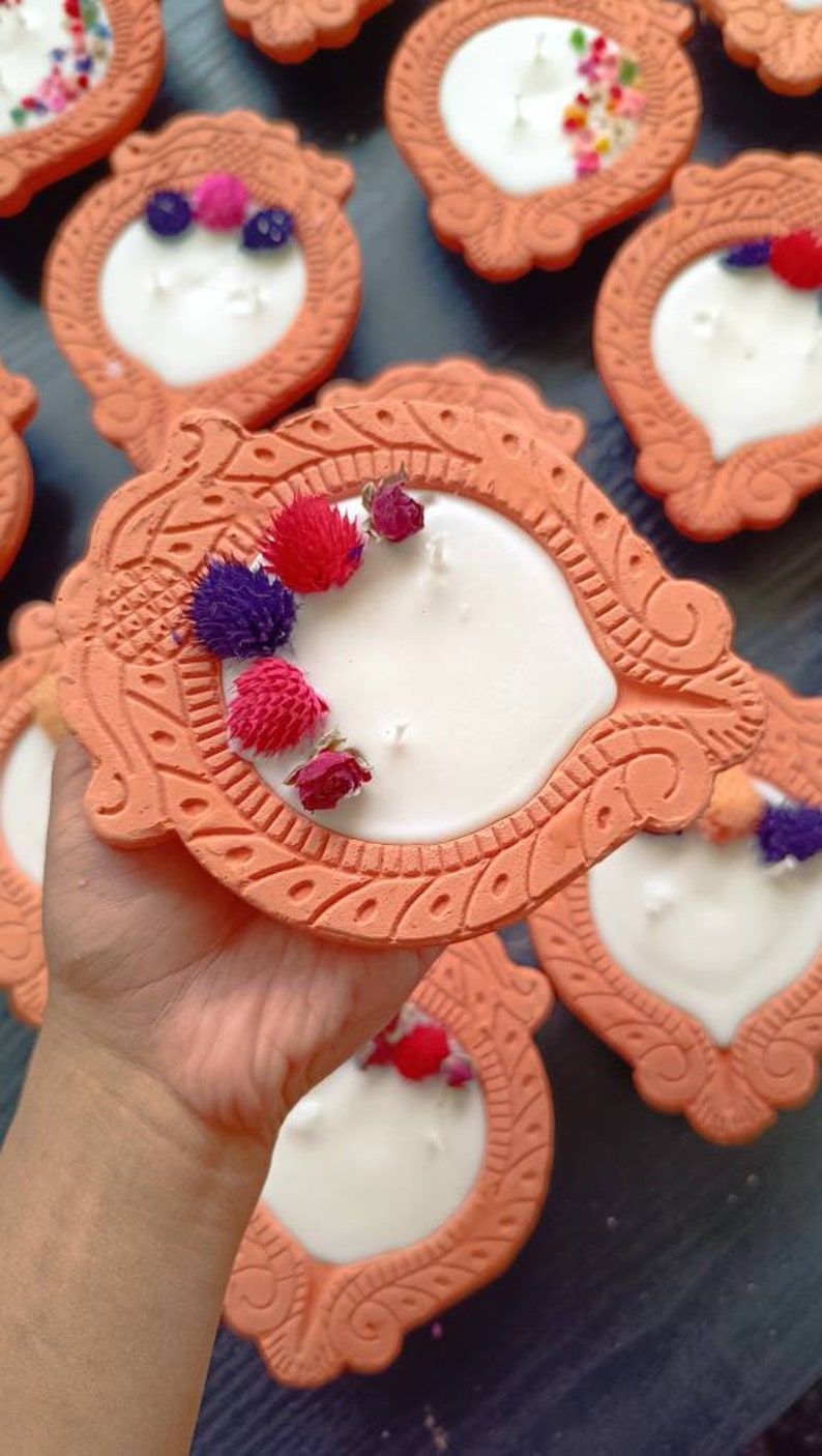 May include: A collection of terracotta candle holders with white candles and dried flower accents. The holders are decorated with intricate designs and have a rustic, earthy aesthetic.