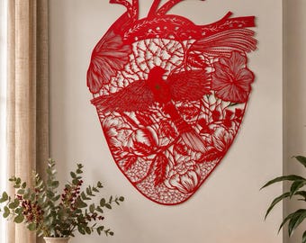 May include: A large, red, laser-cut metal wall art piece shaped like an anatomical heart. The intricate design features a central bird with outstretched wings surrounded by detailed floral patterns, leaves, and vines, creating a complex, lace-like texture.