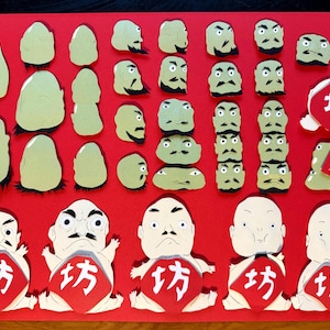 May include: A red background with various green and white paper cutouts of faces and figures. The figures have different facial expressions and some have black hair. There are also red paper cutouts with the Japanese word "KATA" written in white.