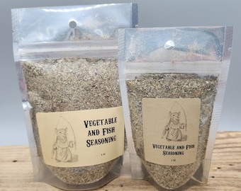 May include: Two clear plastic pouches filled with a blend of dried herbs and spices, labeled "Vegetable and Fish Seasoning." Each pouch has a brown label with a cartoon bear fishing. The pouches are on a wooden surface.