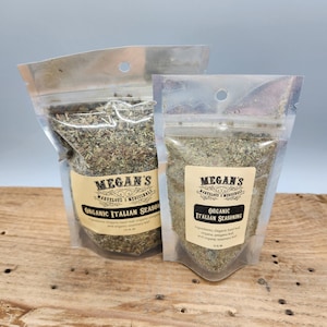 Two clear plastic bags filled with dried herbs, labeled "Megan's Marvelous Medicinals Organic Italian Seasoning". The smaller bag has a label with the ingredients: "Organic basil leaf, organic oregano leaf, and organic rosemary leaf."
