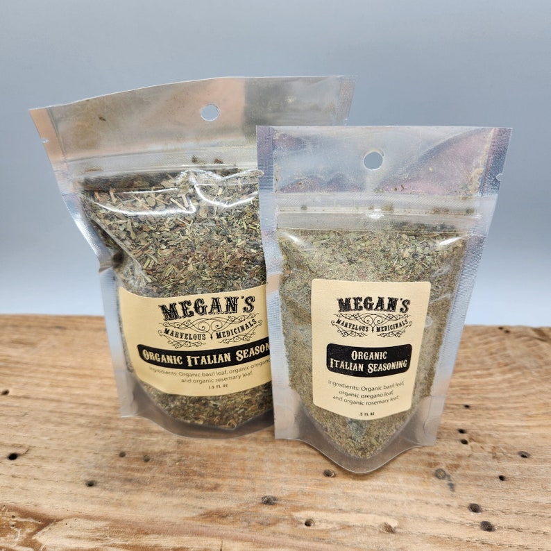 Two clear plastic bags filled with dried herbs, labeled "Megan's Marvelous Medicinals Organic Italian Seasoning". The smaller bag has a label with the ingredients: "Organic basil leaf, organic oregano leaf, and organic rosemary leaf."