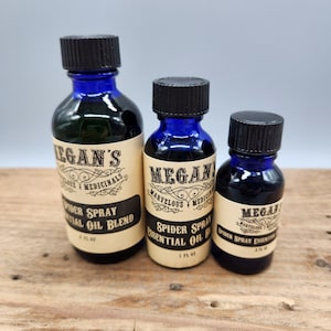 May include: Three blue glass bottles with black lids and labels. The labels are cream colored with black text. The text on the labels reads "Megan's Marvelous Medicinals" and "Spider Spray Essential Oil Blend". The bottles are 2 fl oz, 1 fl oz, and .5 fl oz.