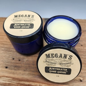 May include: Two 2 ounce jars of mentholated "Goose Grease" with a blue lid and a brown label with the text "Megan's Marvelous Medicinals" and "Mentholated "Goose Grease"".