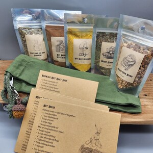 May include: A set of five clear plastic pouches containing various dry seasonings and blends, each with a tan label featuring animal illustrations. A green fabric drawstring bag with a small crocheted acorn charm and several tan recipe cards are included.